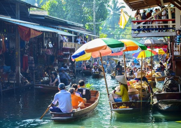 people buying food while while riding small wooden boats at saduak floating market