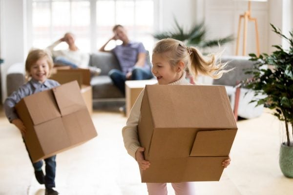 active children enjoying moving day running carrying boxes, excited kids laughing playing in new home while parents take break to rest, happy girl and boy have fun together