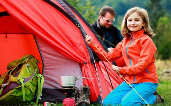 A girl helping her dad set up the tent in a camp site