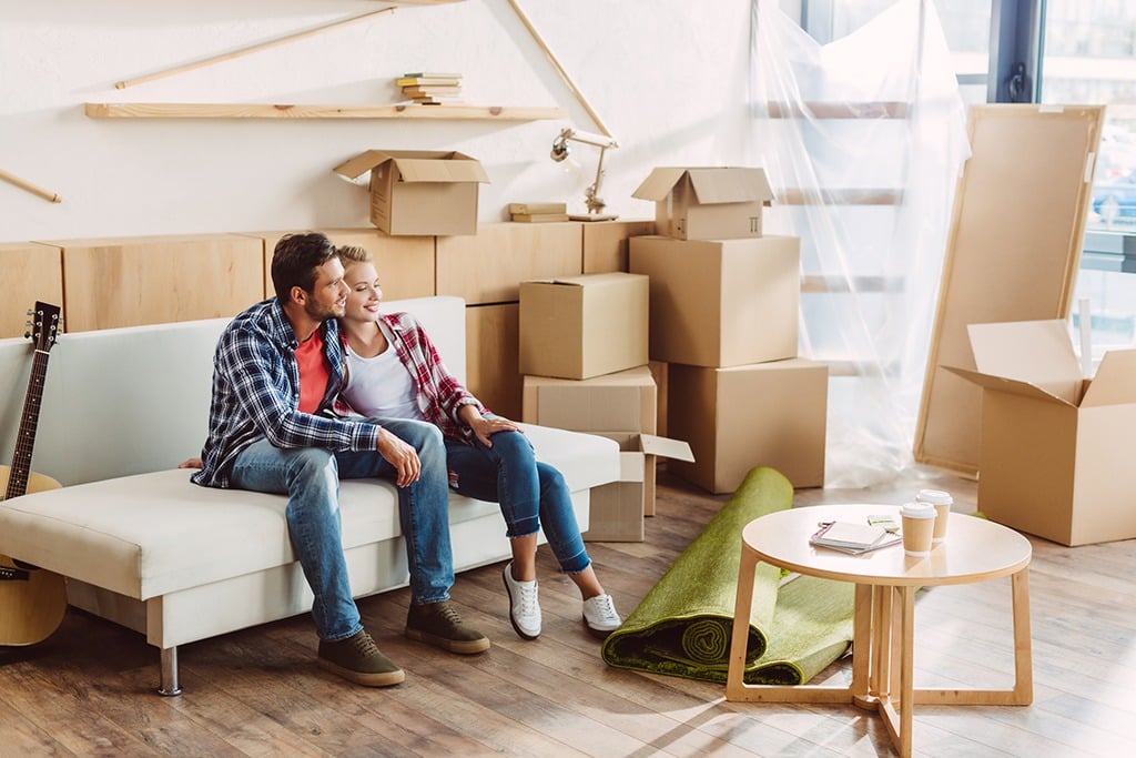 happy young couple sitting together on sofa and looking away in new house