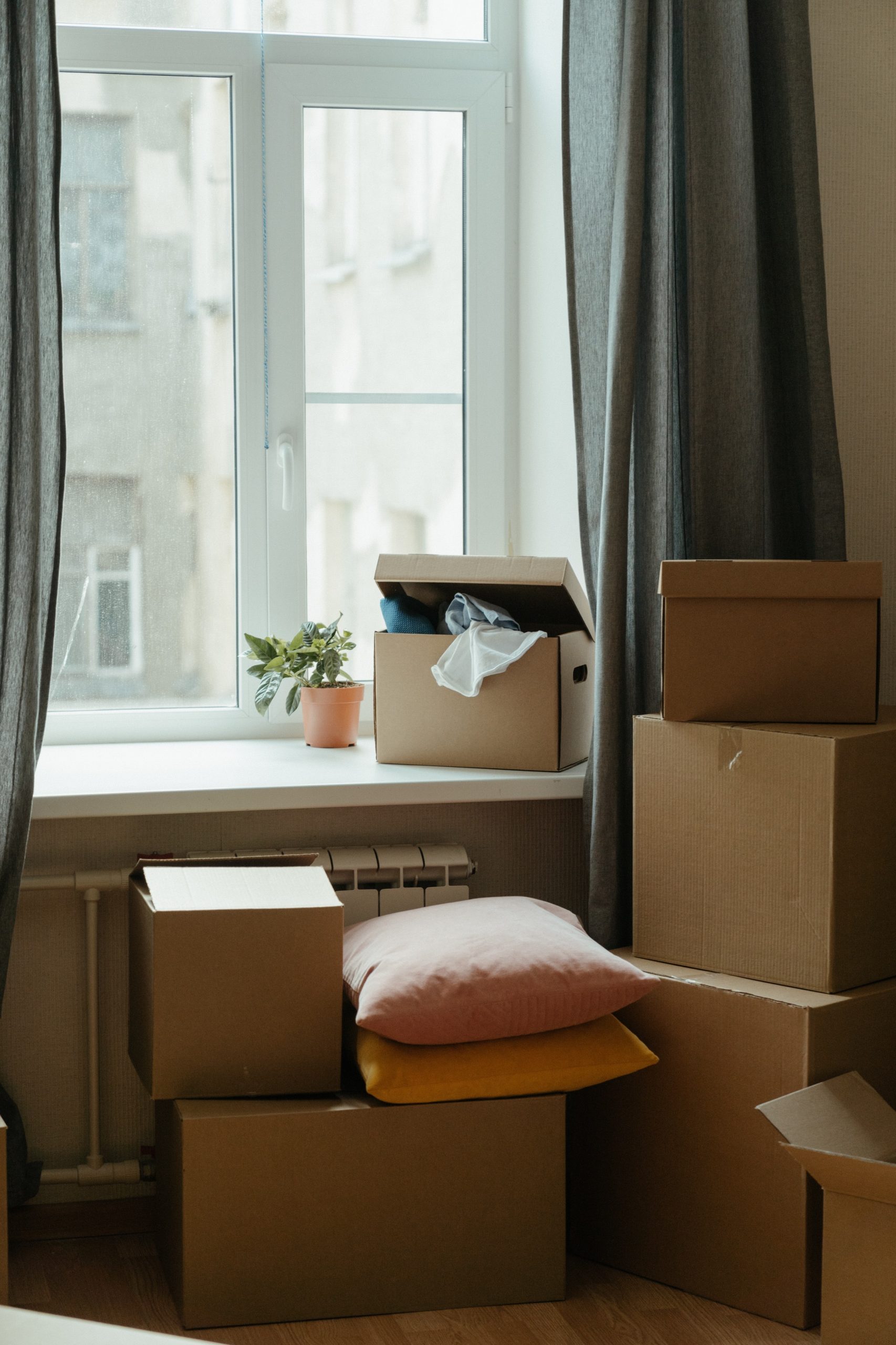 Big window in the middle of the wall with storage boxes everywhere and pillows